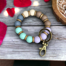 Load image into Gallery viewer, A silicione and wood disc beads wristlet keychain with gold hardware that include a claw clip. The colors are charcoal gray, mint green, lilac, coffee, and cream.