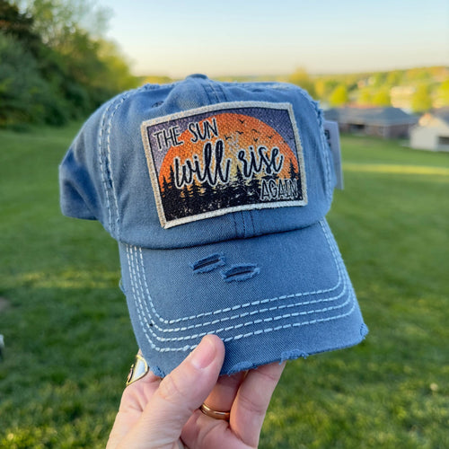 Blue full cotton baseball hat with a frayed edge fabric patch that says, the sun will rise again.