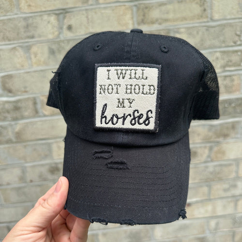 black mesh baseball hat with an embroidered patch that says, "I will not hold my horses". The patch border is black and the words are olive green and black.