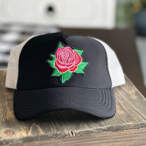 Black front and white mesh back mid profile trucker hat with an embroidered red and pink rose with green leaves patch. The patch has distressed edges.