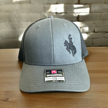 Load image into Gallery viewer, Richardson Lowpro 115 heather gray and black mesh trucker hat with an embroidered cowboy on bucking horse on front left side