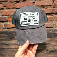 Load image into Gallery viewer, Dark Gray Trucker hat, with a rectangle shaggy edge white patch that says, The best things in life mess up your hair. the patch has a thin black border and frayed edges.