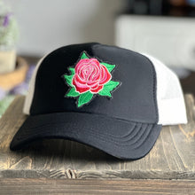 Load image into Gallery viewer, Black front and white mesh back mid profile trucker hat with an embroidered red and pink rose with green leaves patch. The patch has distressed edges.