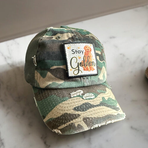 Camo, Stay Golden Patch Hat, Mesh low profile and unstructured trucker hat with distressing. the mesh is hunter green. The patch is square with a black embroidered edge. Stay Golden with a picture of a golden retriever is printed on the patch.
