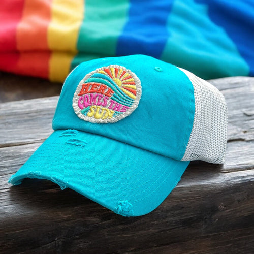 Turquoise and ivory mesh low profile and unstructured trucker hat with a frayed edge embroidered patch that says, here comes the sun.