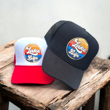Load image into Gallery viewer, Black or a red/white high profile rope trucker hat with a colorful round Lake LIfe graphic printed on the front. Lake life is printed in white cursive bubble font. The colors in the background are in a strip pattern. Blues, yellows, reds