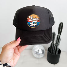 Load image into Gallery viewer, Black high profile rope trucker hat with a colorful round Lake LIfe graphic printed on the front. Lake life is printed in white cursive bubble font. The colors in the background are in a strip pattern. Blues, yellows, reds