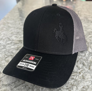 Black and charcoal mesh Richardson Low Pro 112 Trucker hat with an embroidered cowboy riding a bucking bronco. The thread is black making it tone on tone.