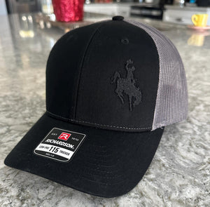 Black and charcoal mesh Richardson Low Pro 112 Trucker hat with an embroidered cowboy riding a bucking bronco. The thread is black making it tone on tone.