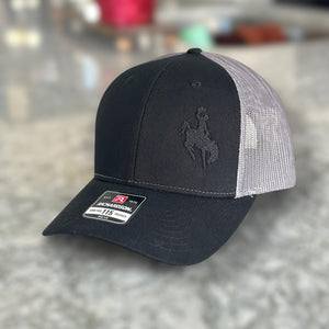 Black and charcoal mesh Richardson Low Pro 112 Trucker hat with an embroidered cowboy riding a bucking bronco. The thread is black making it tone on tone.