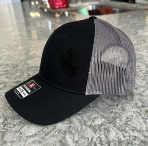 Black and charcoal mesh Richardson Low Pro 112 Trucker hat with an embroidered cowboy riding a bucking bronco. The thread is black making it tone on tone.