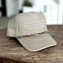 Load image into Gallery viewer, Tan trucker hat with the phrase, If you&#39;re hanging on by a thread, make sure it&#39;s the hem of His garment. matthew 9:20-22. It in white font