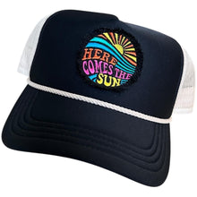 Load image into Gallery viewer, A black mid profile trucker hat with a cream rope and cream mesh. It has an embroidered here comes the sun round raggy patch. The image is embroidered onto a black frayed fabric using bright colors of orange pink, yellow, blue and teal.