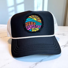 Load image into Gallery viewer, A black mid profile trucker hat with a cream rope and cream mesh. It has an embroidered here comes the sun round raggy patch. The image is embroidered onto a black frayed fabric using bright colors of orange pink, yellow, blue and teal.