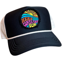 Load image into Gallery viewer, A black mid profile trucker hat with a cream rope and cream mesh. It has an embroidered here comes the sun round raggy patch. The image is embroidered onto a black frayed fabric using bright colors of orange pink, yellow, blue and teal.