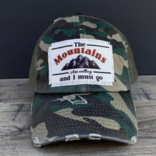 Load image into Gallery viewer, A mesh camo trucker hat with a raggy patch that says, The mountains are calling and I must go. Low profile and unstructured.