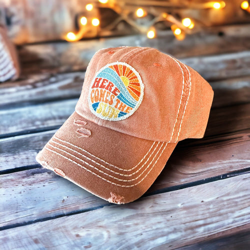 Here Comes the Sun raggy fabric hat patch, in circle shape (2.5 inches) on a rusty orange cap with white stitching. The patch colors are three shades of blue, orange, redish orange, and yellow. Gorgeous patch!
