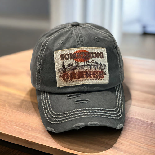 Dark gray baseball hat with white stitching. It has a rectangle light tan patch that is frayed around the edges. It has a western desert scene with the words, Something in Orange tell me we're not done.