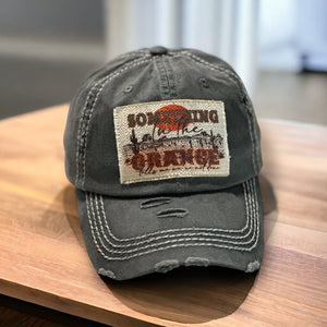 Dark gray baseball hat with white stitching. It has a rectangle light tan patch that is frayed around the edges. It has a western desert scene with the words, Something in Orange tell me we&#39;re not done.