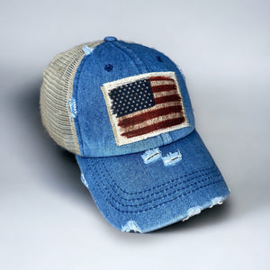 Denim blue high ponytail hat with tan mesh back. Velcro strap. The hat is distressed and has a raggy edge patch with a.vintage American flag patch.